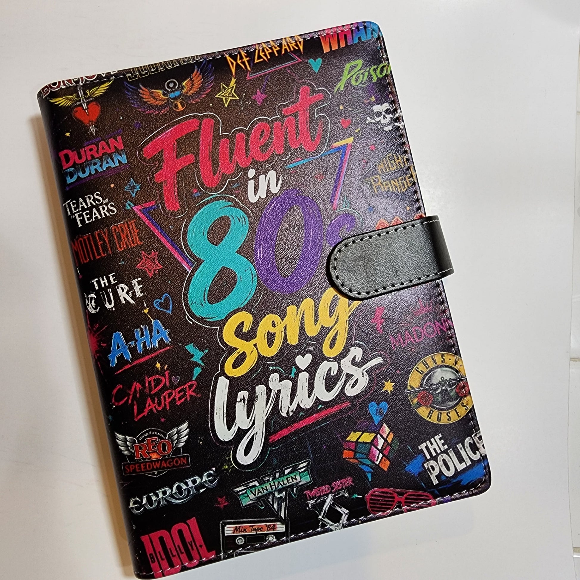A black faux-leather passport cover featuring a colorful 1980s song lyrics collage design with various music artist names and graphics.