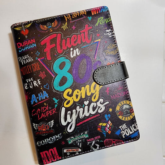 A black faux-leather passport cover featuring a colorful 1980s song lyrics collage design with various music artist names and graphics.